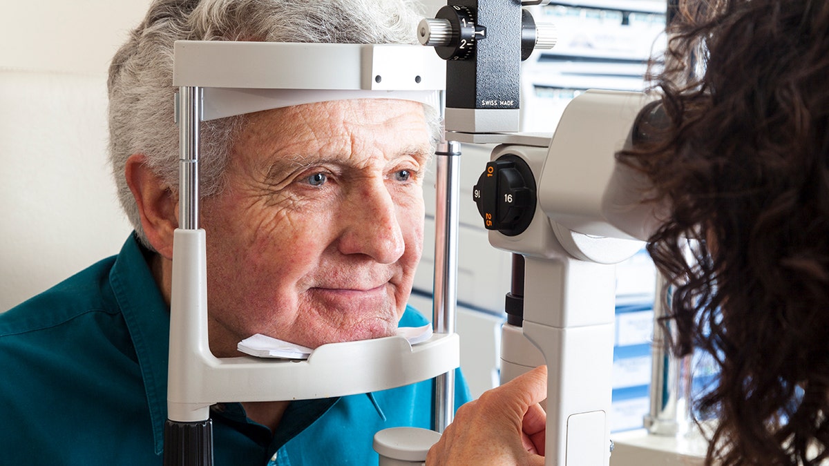 Optometrist giving eye exam to senior man seated in exam chair