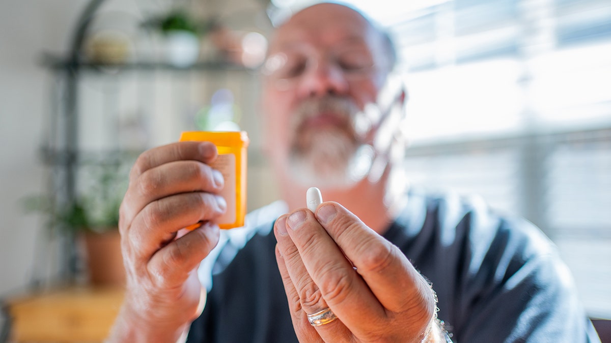 senior man holds one white pill and pill bottle