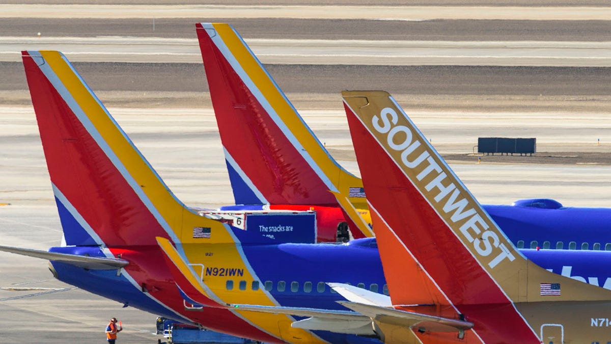 Southwest Airlines planes are seen parked at an airport, with their red, yellow and blue tail fins lined up on the tarmac.