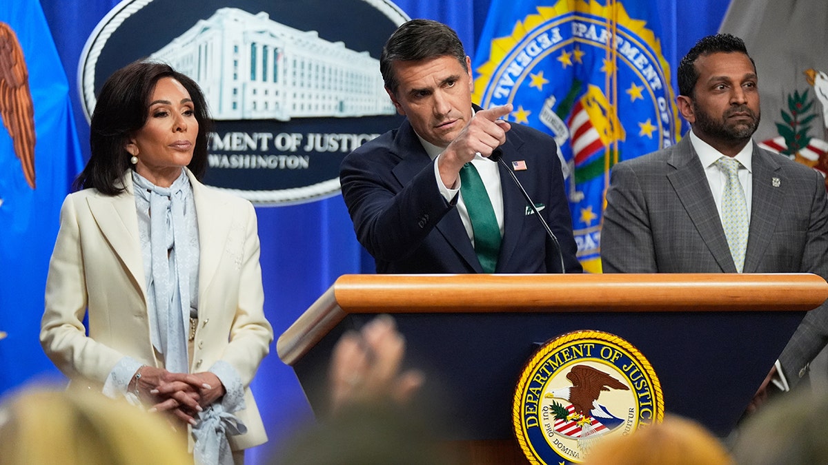 Todd Blanche speaking at a lectern flanked by Jeanine Pirro and Kash Patel.