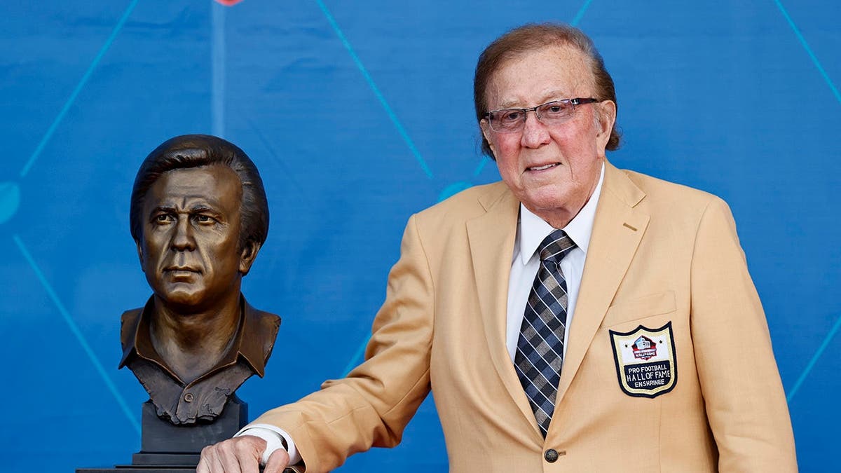 Tom Flores posing with his bust at the Pro Football Hall of Fame induction ceremony in Canton, Ohio.
