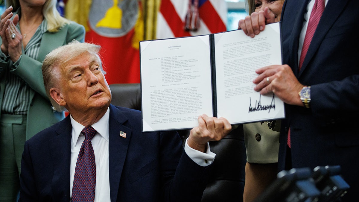 Donald Trump handing a signed presidential memorandum to Senators Marsha Blackburn and Bill Hagerty in the Oval Office
