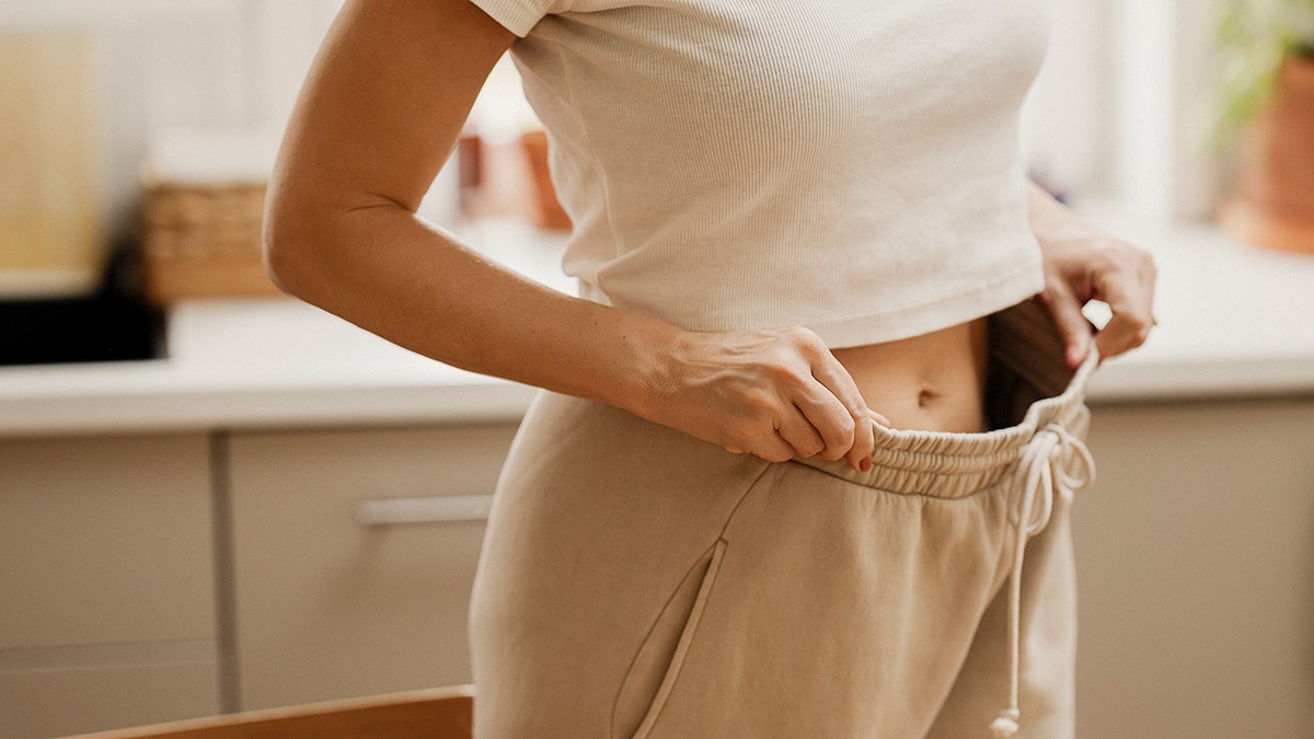A woman holding her sweatpants out to show weight loss