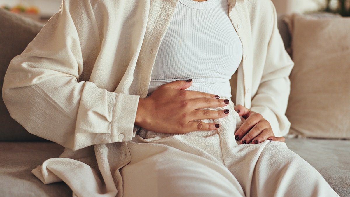 Woman holding stomach and hands in pain sitting on sofa