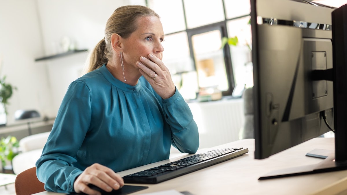 A woman in a blue blouse working on a desktop in a home office.