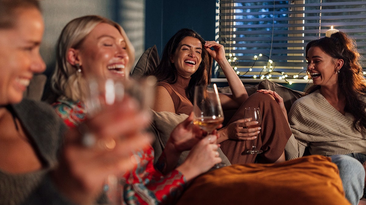 Group of women sitting on a sofa drinking wine and laughing