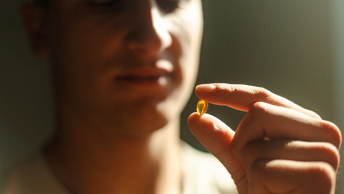 A man holding a yellow capsule between two fingers in sunlight.