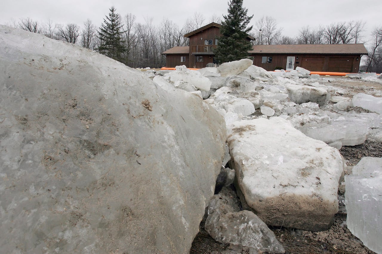 Blocks of ice are seen piled up on a river with a house in the background.
