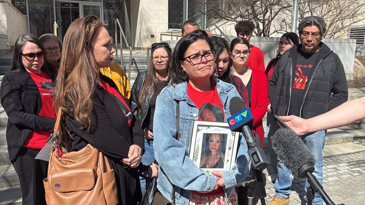 A woman stands with many supporters behind her. She is holding a photo of a young woman.
