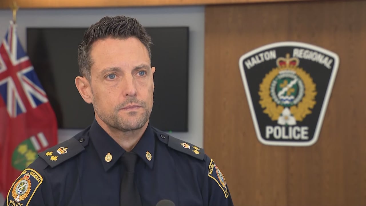 A man in a police uniform stands in front of a Halton Regional Police Service sign.
