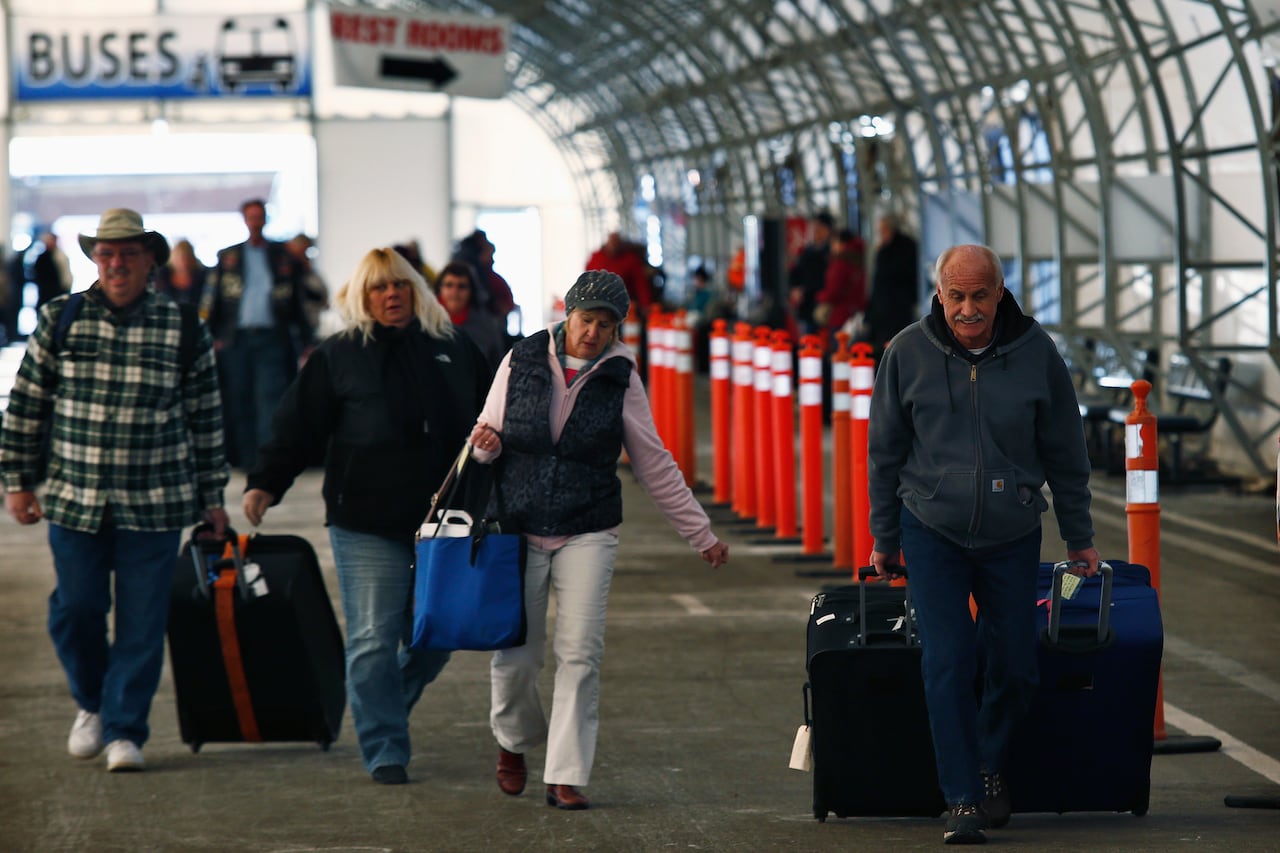 People with rolling suitcases walk away from a cruise ship