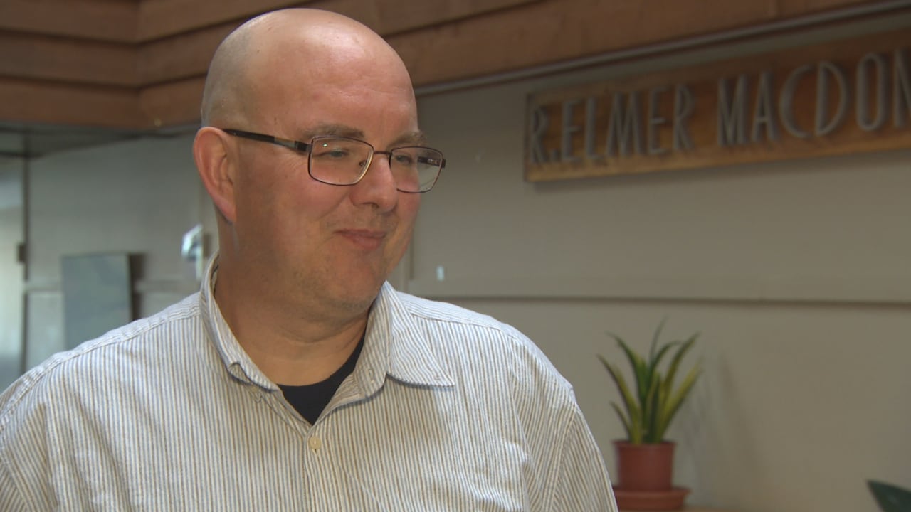 a bald man with glasses stands indoors