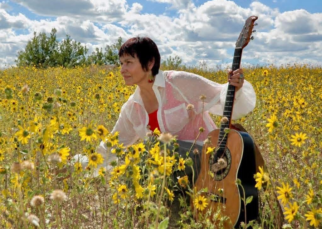 A woman holding a guitar in a field of sunflowers
