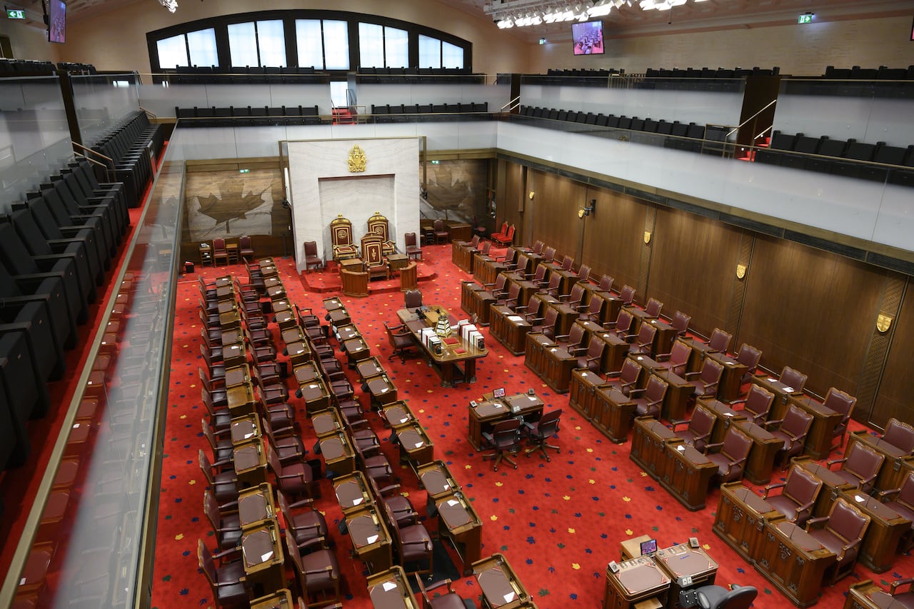 A row of desks in a red carpetted legislative chamber sit empty.