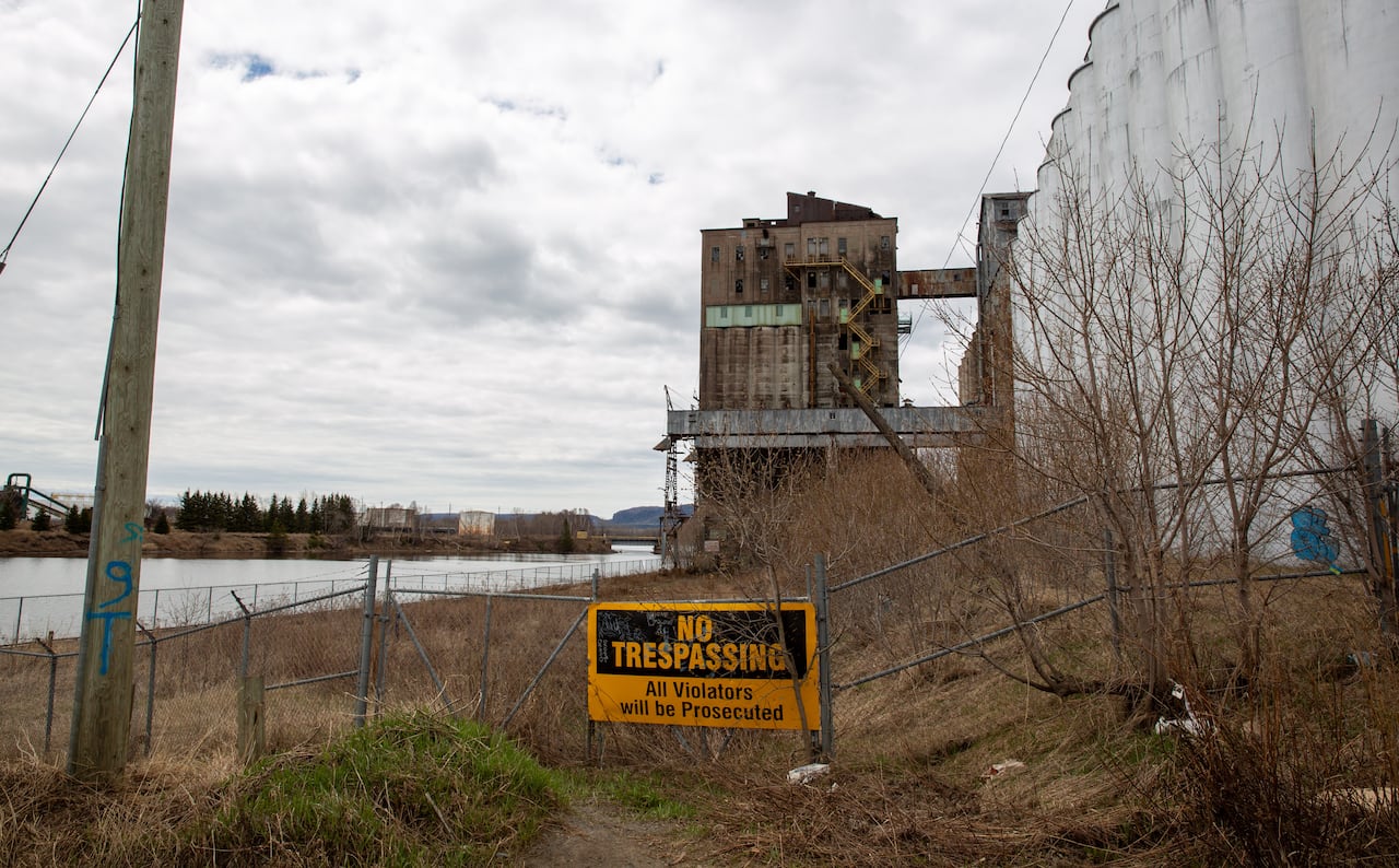 A wide shot of abandoned grain elevators seen behind a fence.