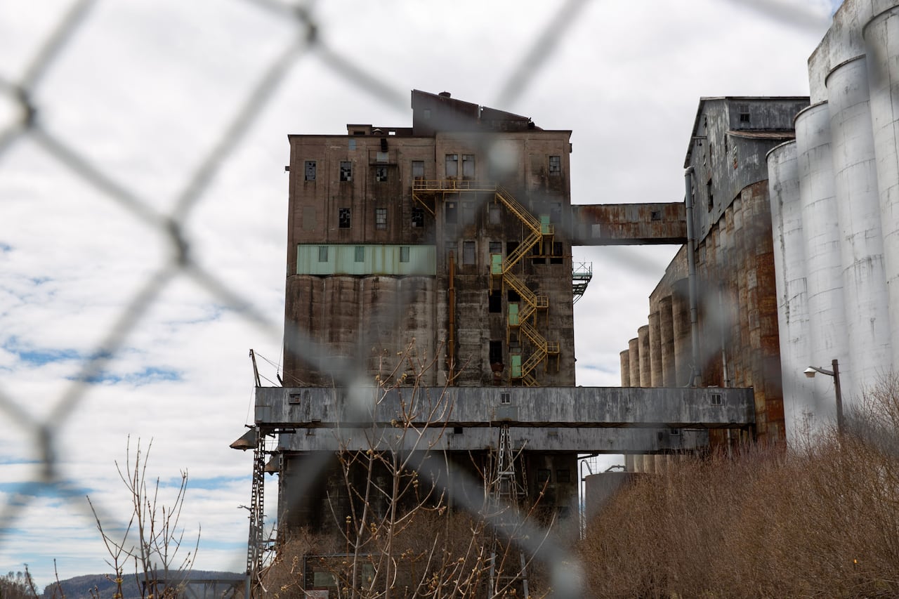 Abandoned grain elevators are seen behind a chain-link fence.
