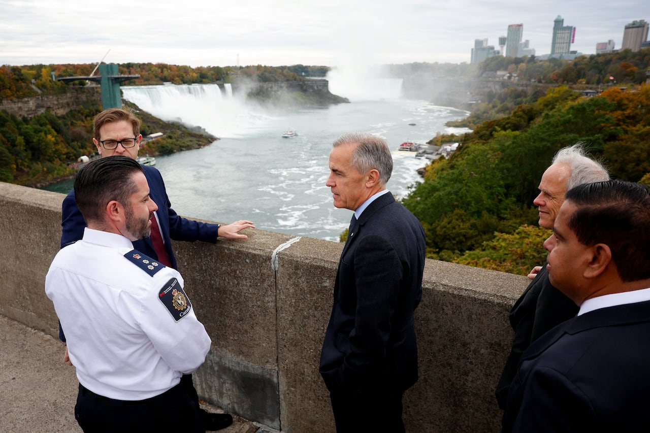 Men stand in suits and law enforcement uniforms stand on a bridge overlooking a waterfall.