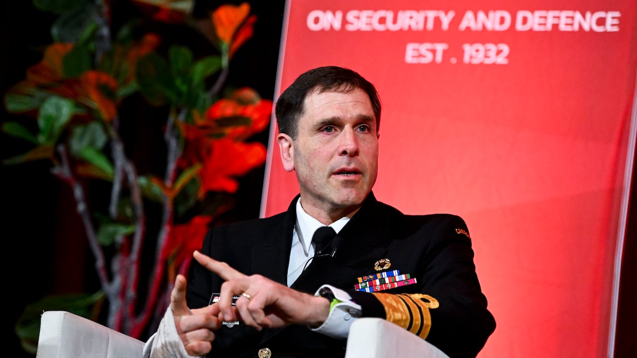 A man in a navy uniform sitting in a chair on stage.