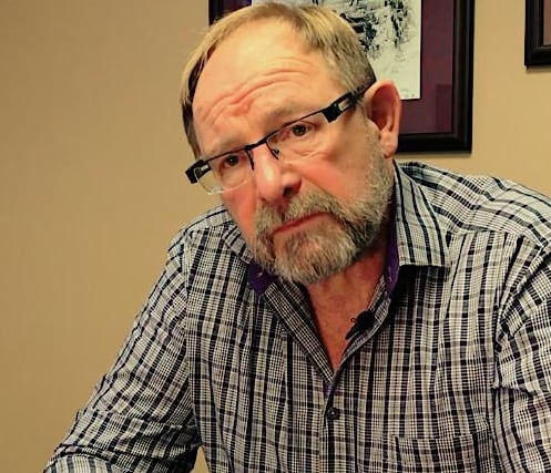 A white man wearing a checked shirt poses for a picture.