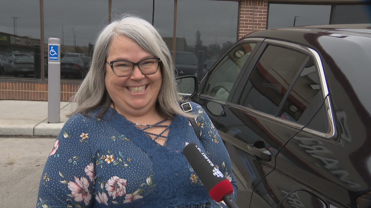 A woman smiles outside of a store entrance.