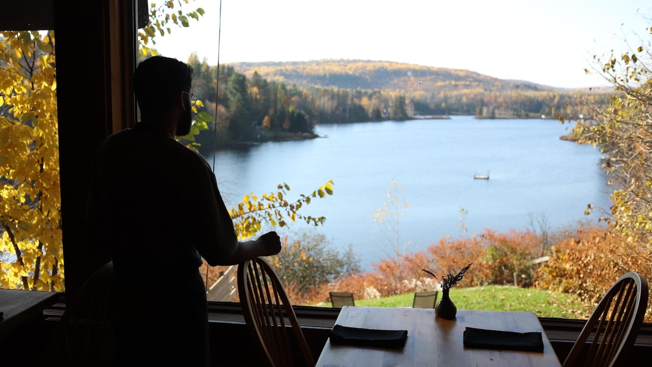 A person inside a restaurant looking at a lake nearby through the window.