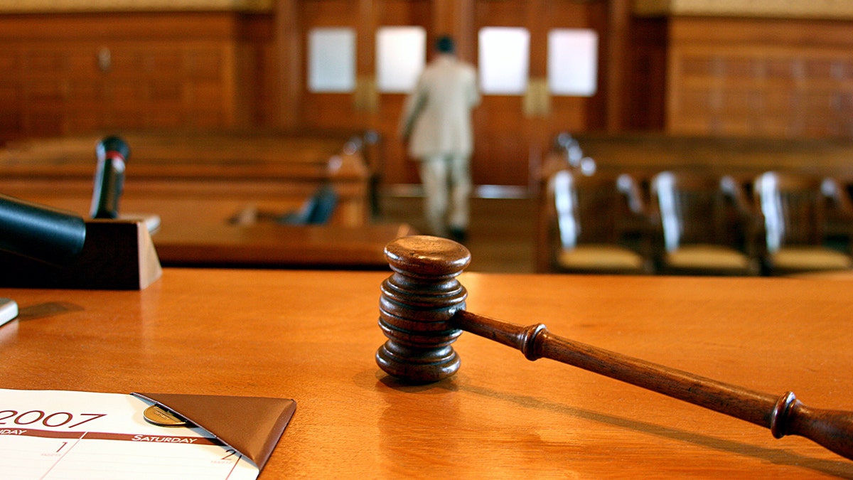 A gavel resting on a judge's bench in a courtroom as people leave