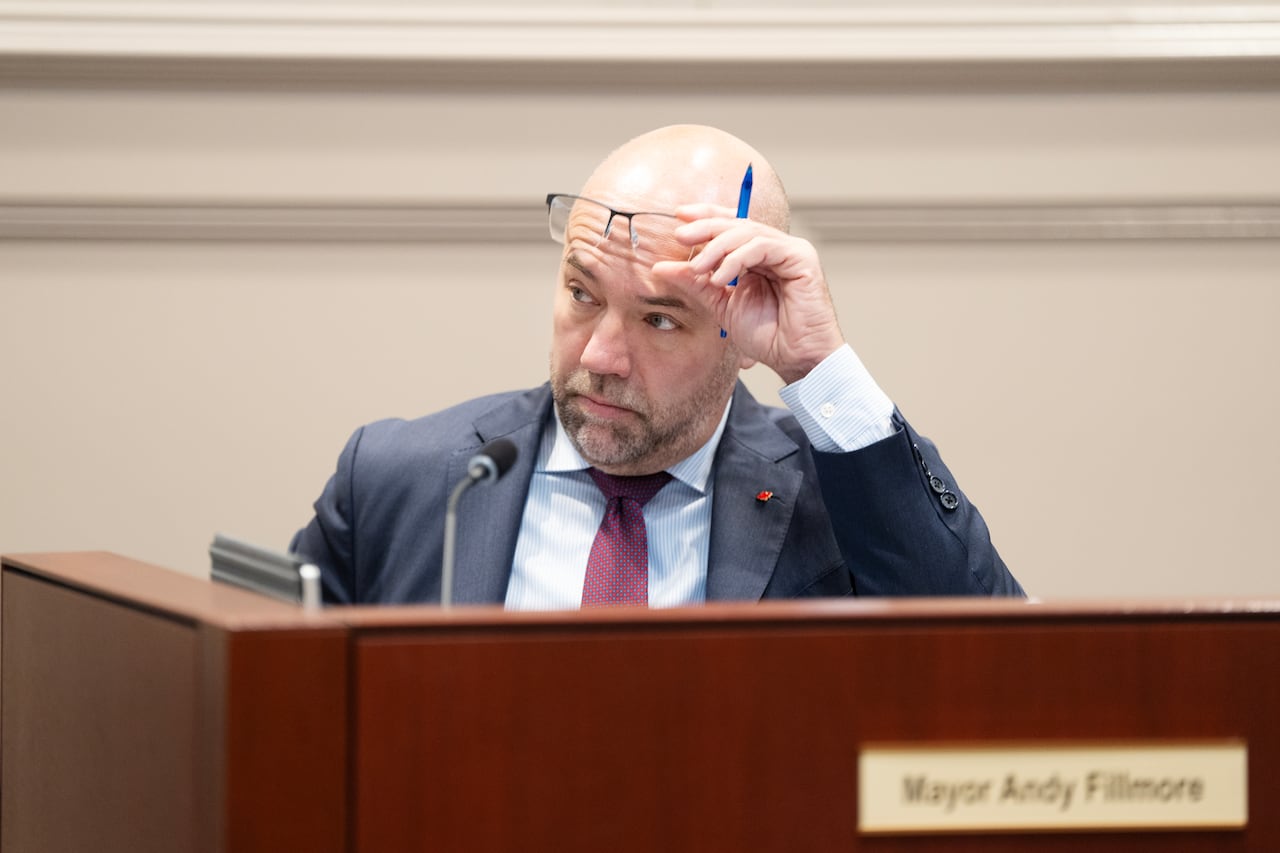 Man holds his glasses up while seated at a desk