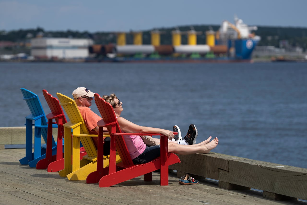 A man and woman seated in colourful Adironak chairs by the water
