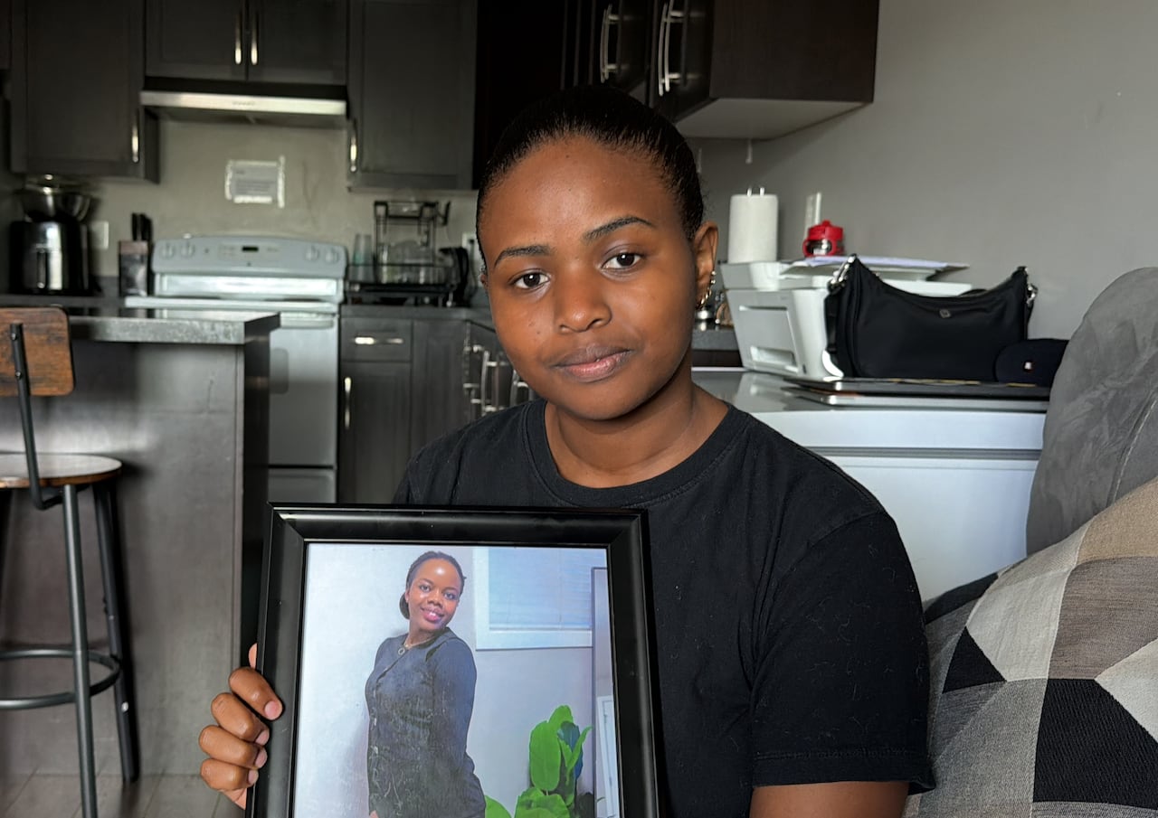 A Black woman holds up a picture of another Black woman in a kitchen.