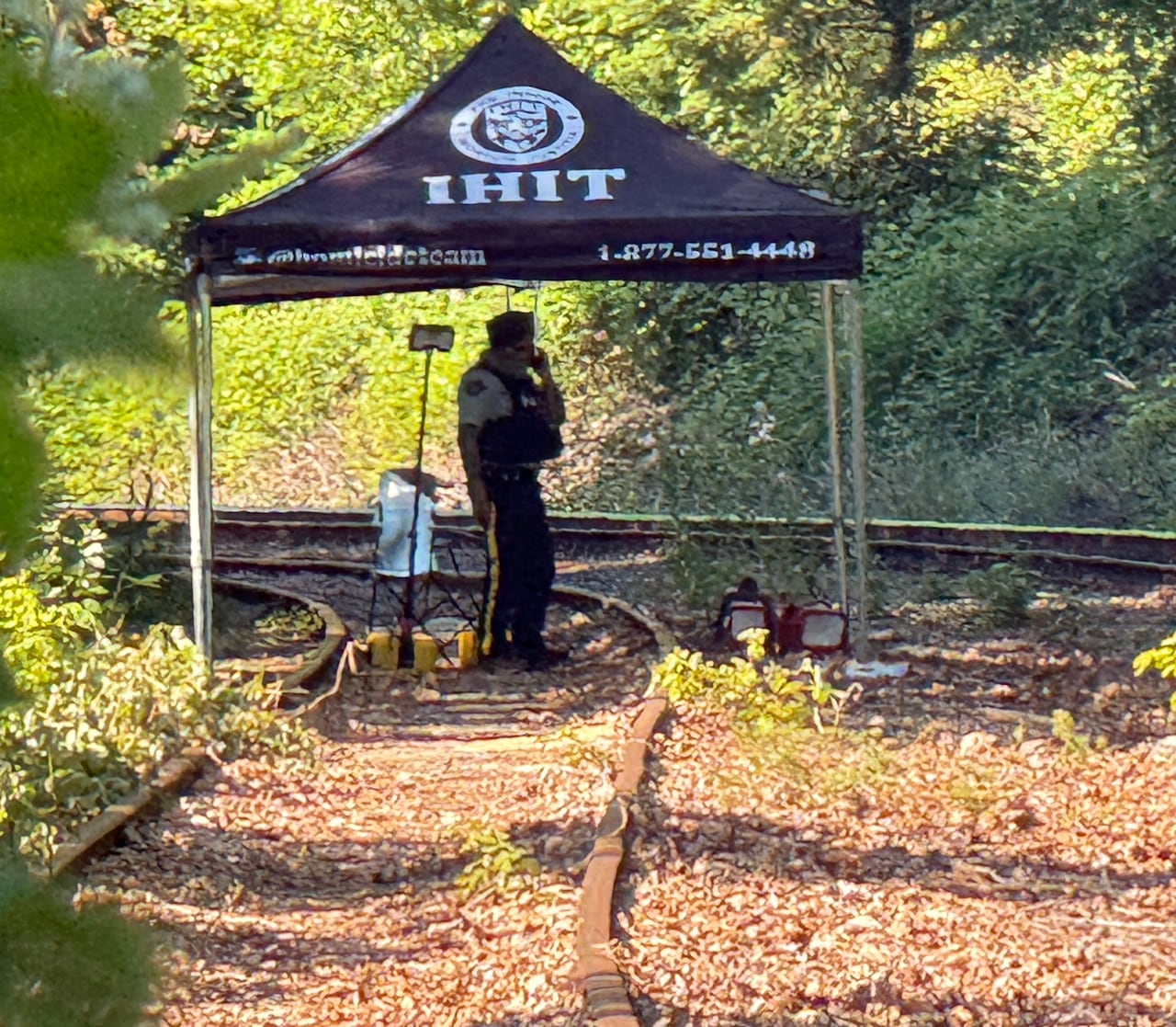 A tent with the words 'IHIT' on it on train tracks, with a police officer underneath it.