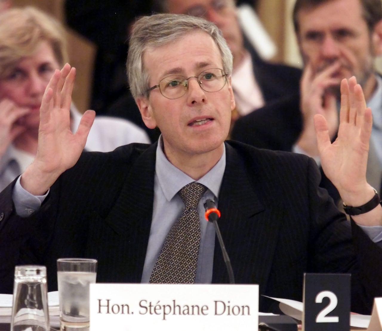 A man in a suit raises his hands in the air to emphasize a point while he speaks.