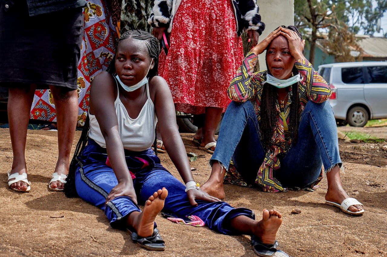 Two women cry while sitting on the ground outside