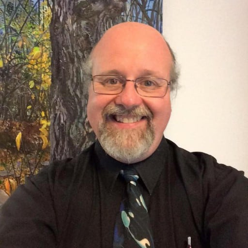 A man in a black shirt and glasses smiles at the camera.