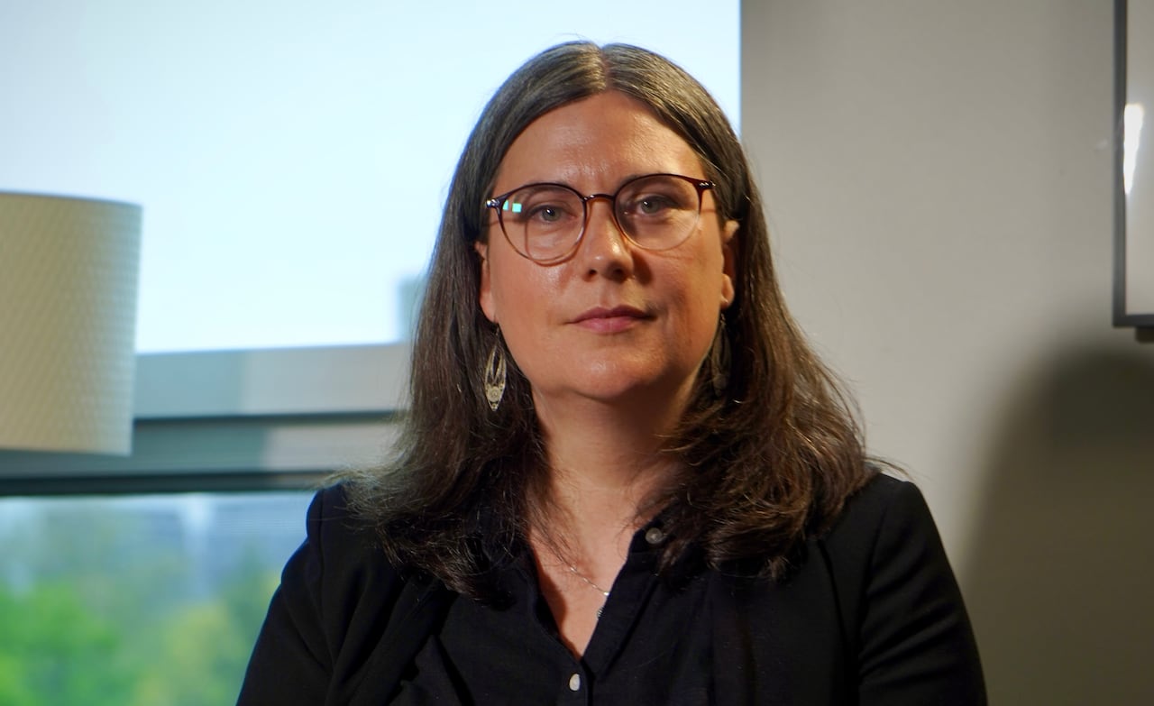A woman in glasses looks at the camera