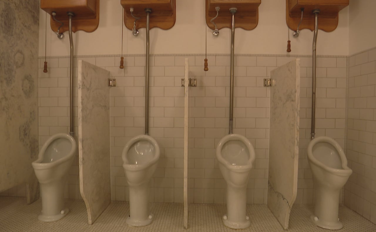 A row of white ceramic urinals in front of a white-tiled wall with white marble partitions between them.
