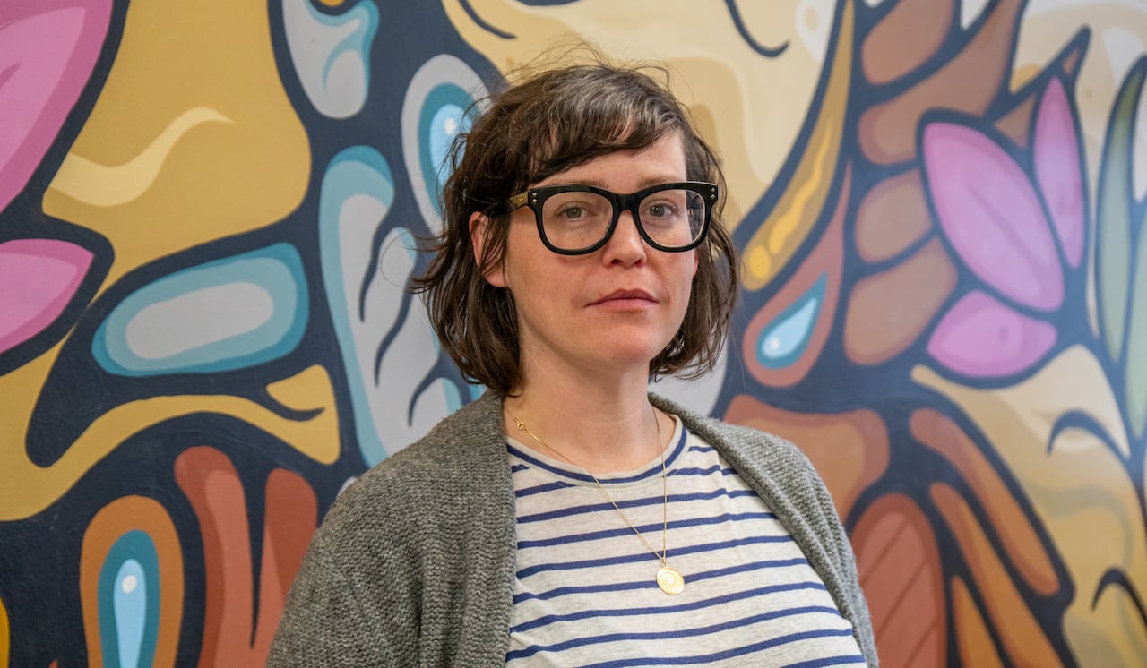 A person stands in front of a multi-coloured wall mural.