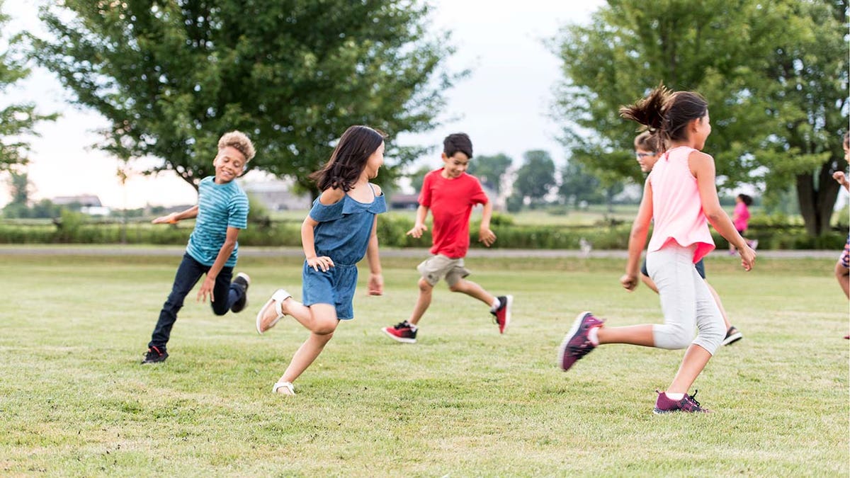 A multi-ethnic group of elementary school students playing tag outside on grass