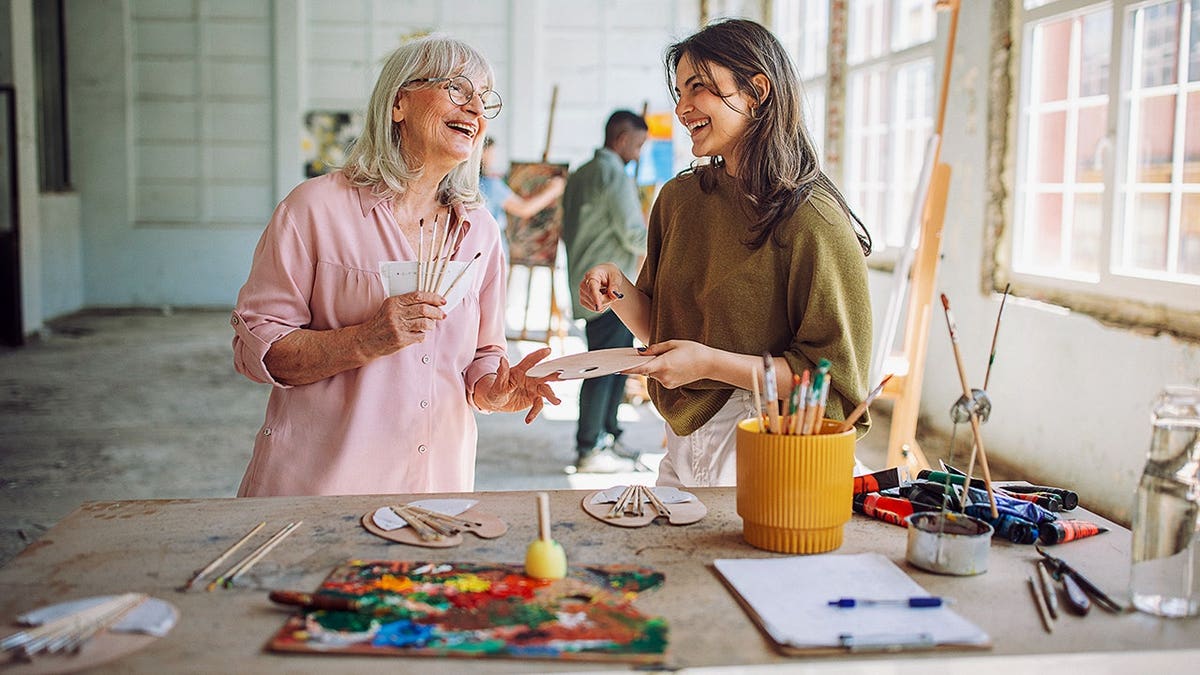 Art teacher laughing alongside a student in a sunlit studio