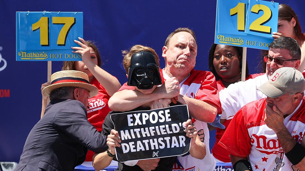 Joey Chestnut grabbing a protester by the neck at Nathan's Hot Dog Eating Contest in Coney Island