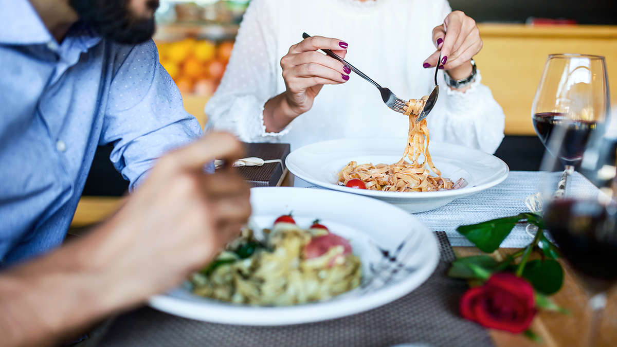 man and woman with forks in pasta dishes at restaurant