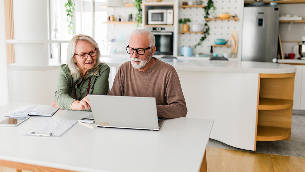 Senior couple sitting at kitchen table using laptop to plan home budget