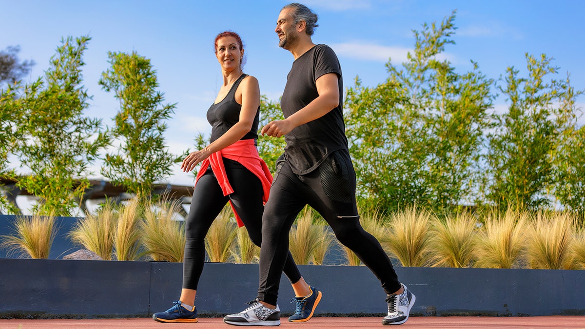 A man and woman walking together along a tree-lined path
