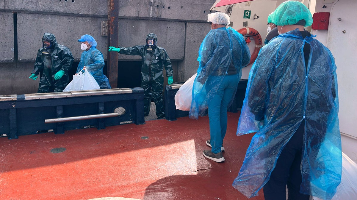 Passengers in blue protective gowns and hair nets disembarking from cruise ship at port
