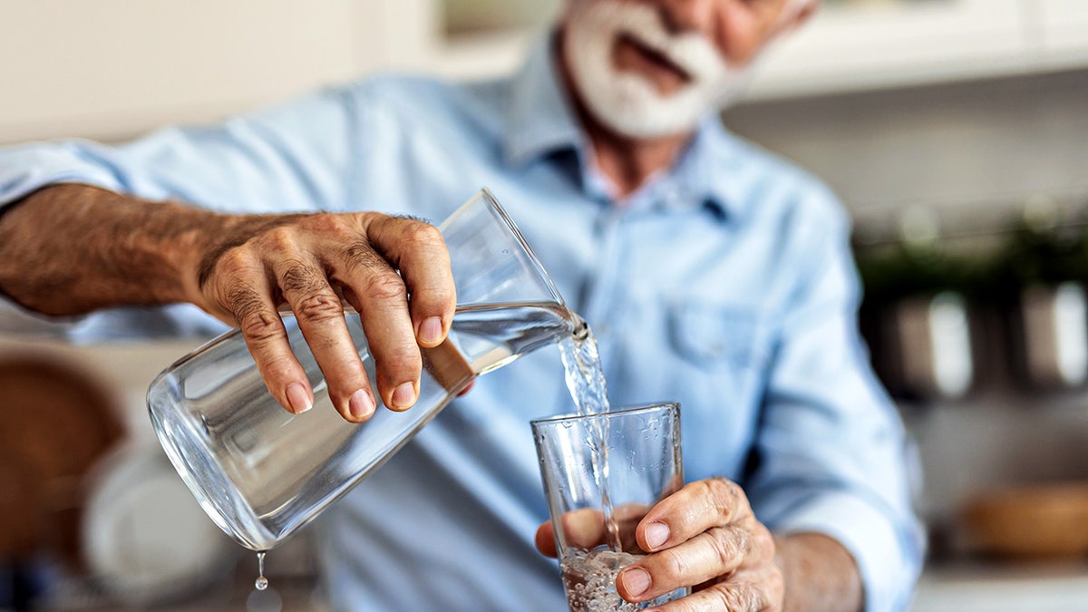 Senior man pouring water from a jug into a glass in a kitchen