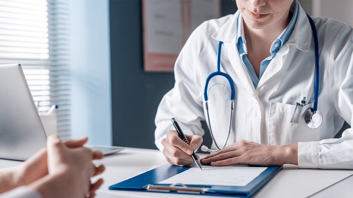 Doctor sitting at desk writing a prescription.