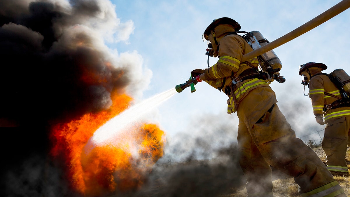 Firefighters holding a fire hose extinguishing a fire.