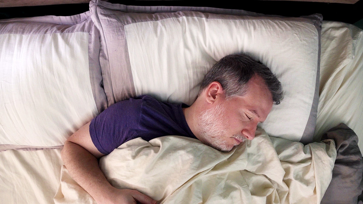 Man sleeping on his back in bed at dawn