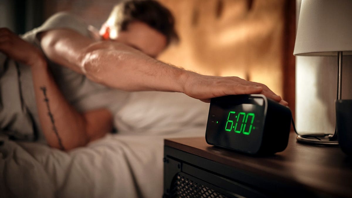 Man turning off alarm clock in bed in bedroom apartment