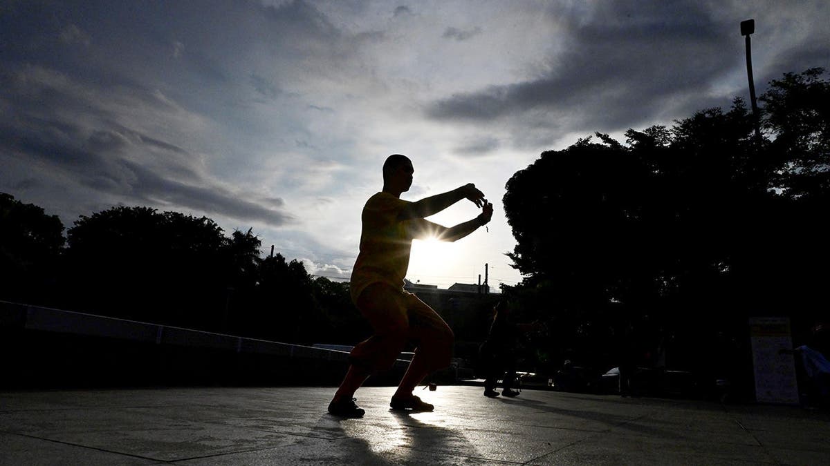 A man practices baduanjin outside as the sun sets.