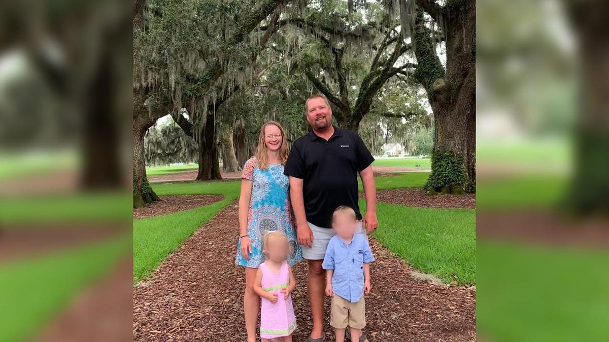 A family of four smiles in front of trees.